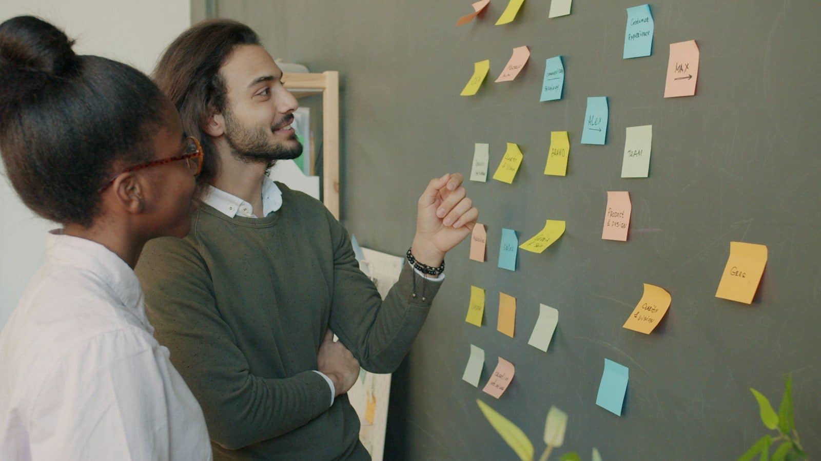 Two colleagues discuss sticky notes on a wall